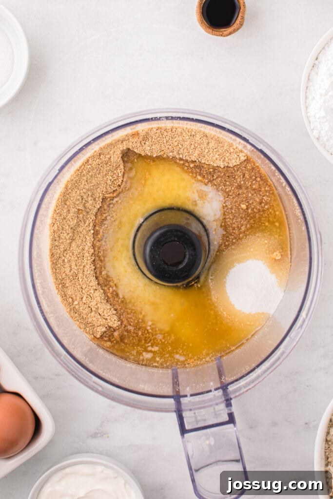 Food processor filled with graham cracker crumbs, granulated sugar, and melted butter before pulsing for the crust.