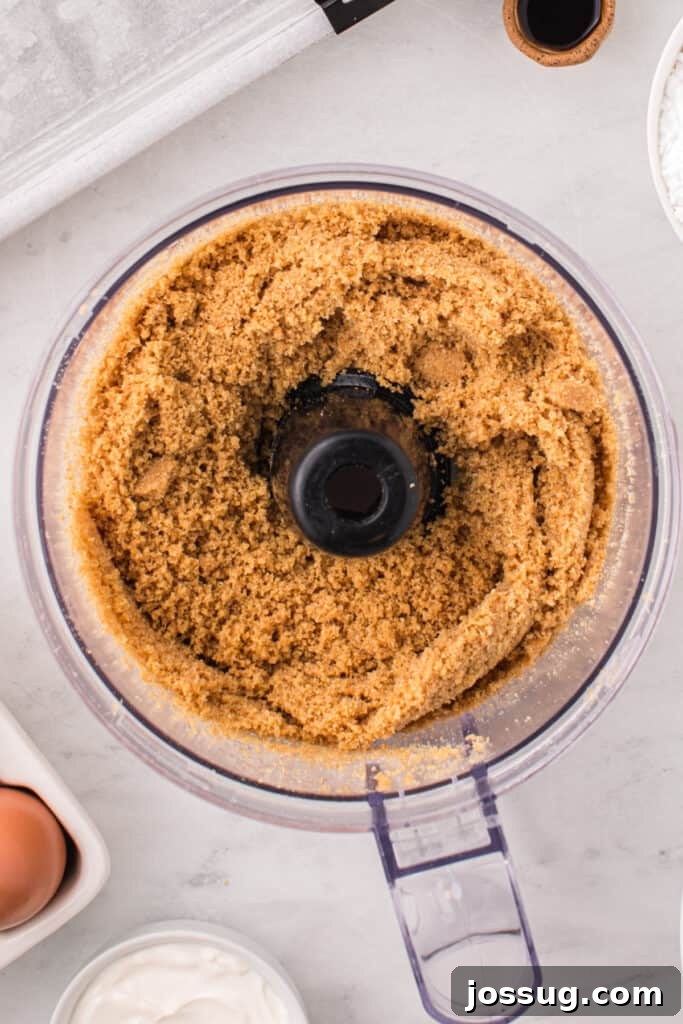 Crumbly graham cracker crust mixture in a food processor after pulsing, showing the correct consistency.