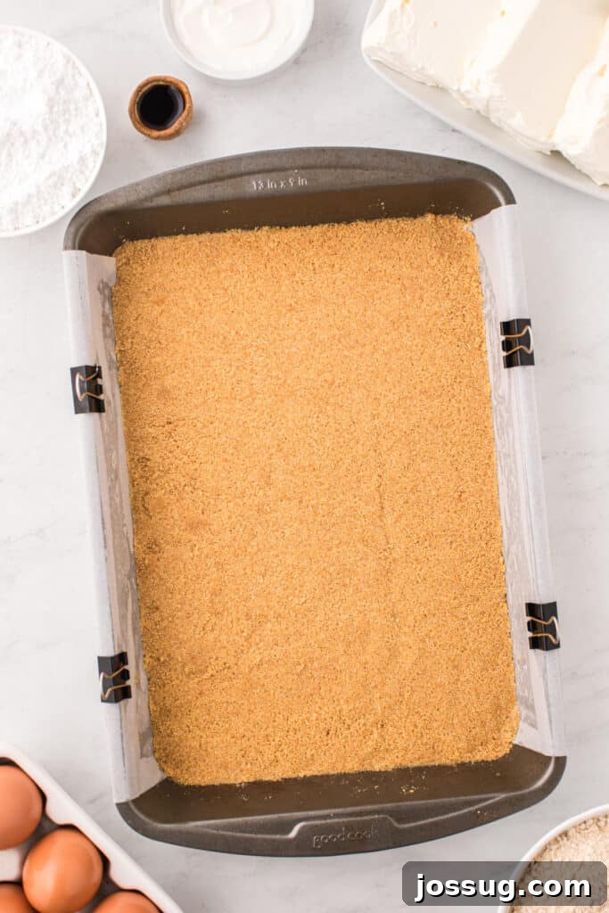 Pressed graham cracker crust in a parchment-lined 9x13-inch baking pan, forming a solid base.