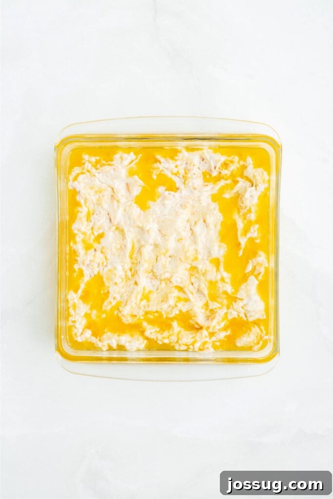 Biscuit dough evenly spread into the melted butter in a square baking dish, ready for scoring.