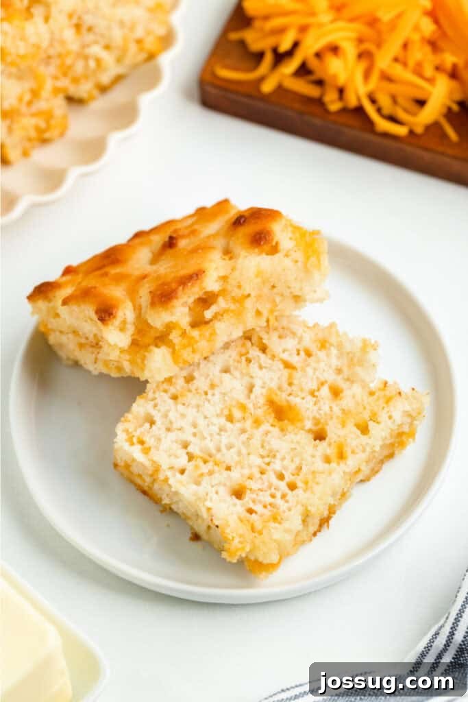 A single biscuit sliced in half on a plate, revealing its irresistible fluffy texture and melted cheddar cheese inside.