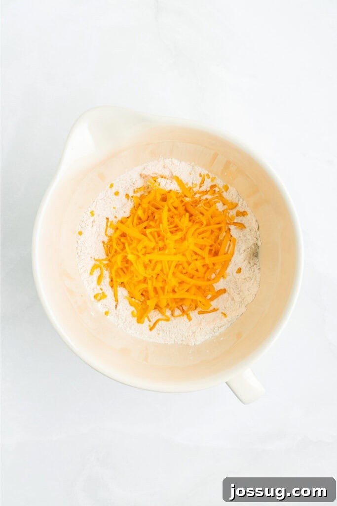 Generous amount of shredded cheddar cheese added to the dry flour mixture in a large mixing bowl, ready for combining.