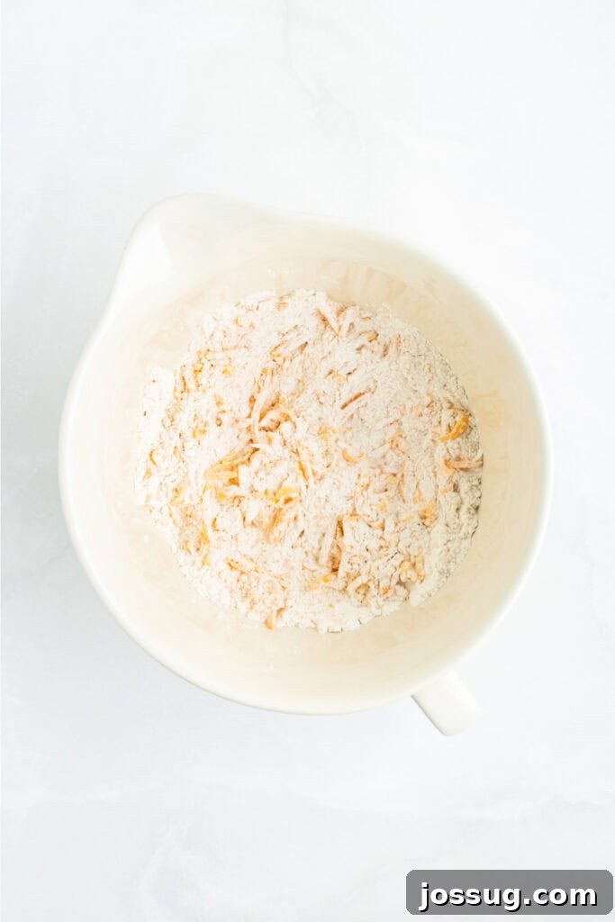 Flour mixture combined with shredded cheddar cheese, creating a uniform mixture before the addition of liquid.