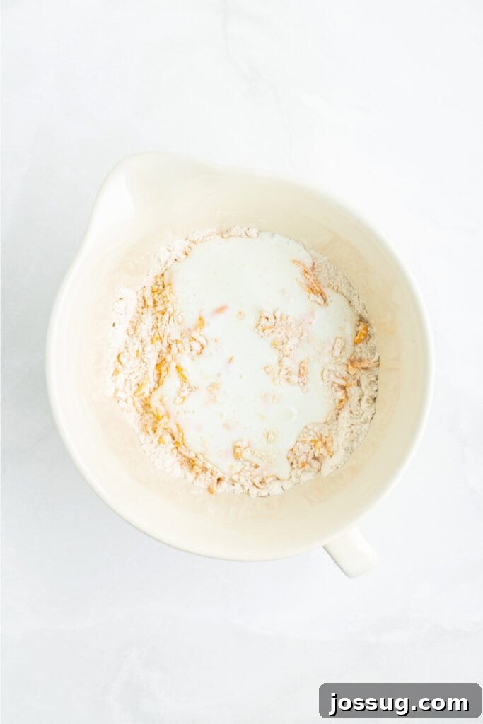 Buttermilk poured into the bowl containing the flour and cheddar mixture, beginning to form the biscuit dough.