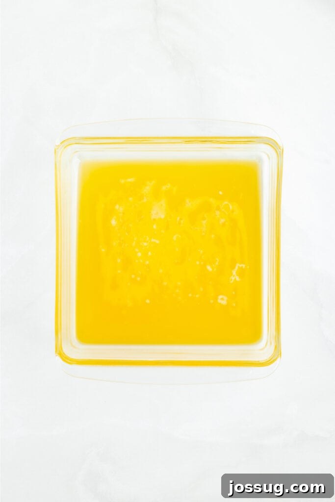 Square baking dish filled with a generous layer of melted butter, serving as the 'swim' for the biscuit dough.