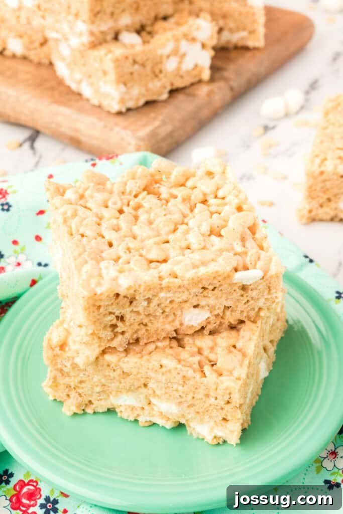 Caramelized Butter Rice Crisps 2 Two stacked Browned Butter Rice Crispy Treats on a green plate with more bars in the background on a wooden board.