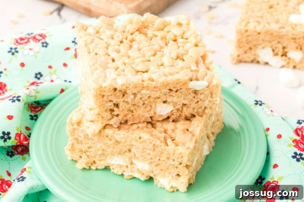 Caramelized Butter Rice Crisps 13 Close-up of two Browned Butter Rice Crispy Treats stacked on a green plate with a floral cloth and extra bars in the background.
