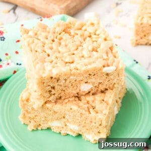 Square crop of two thick, gooey Browned Butter Rice Crispy Treats stacked on a green plate with visible marshmallow pockets.