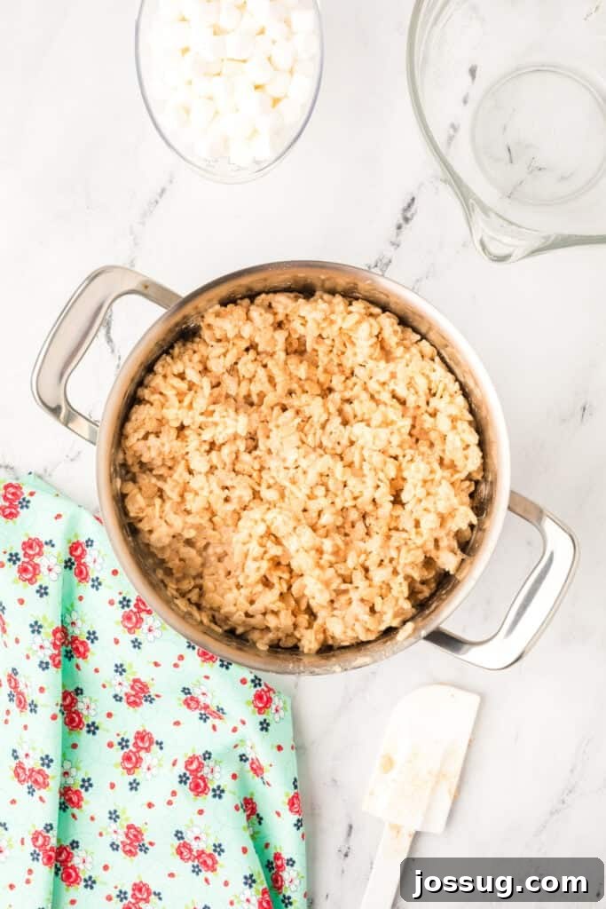 Caramelized Butter Rice Crisps 9 Mixture of crispy rice cereal and melted marshmallows being stirred together in a large stainless steel pot.