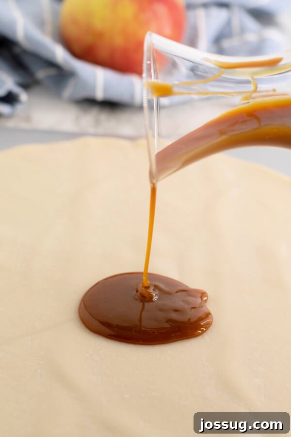 Thick, golden caramel sauce being poured generously over an unrolled pie crust on a baking sheet.