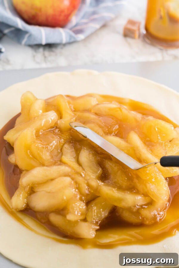Apple pie filling being spread over the caramel layer on the pie crust, leaving a border.