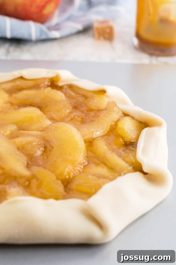 The pie crust edges are neatly folded over the apple and caramel filling, creating a rustic look before baking.