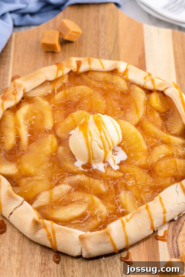 A beautifully finished Caramel Apple Galette, served with a melting scoop of vanilla ice cream, on a rustic wooden cutting board.