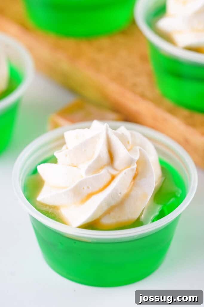 Close-up of a finished caramel apple jello shot topped with a generous swirl of whipped cream and a luscious caramel drizzle.