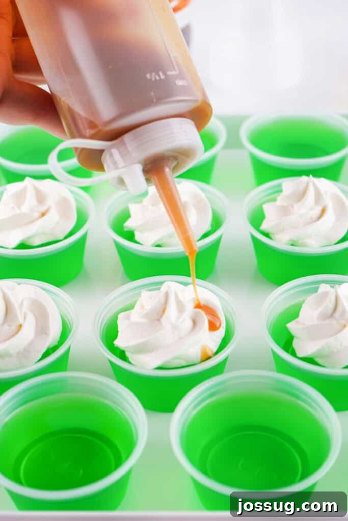 Caramel sauce being drizzled over whipped topping on finished caramel apple jello shots.