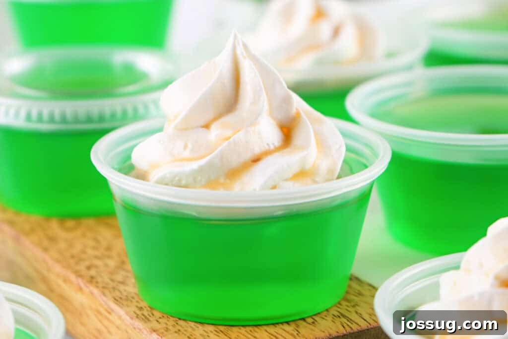 Close-up of a single green jello shot topped with whipped cream and caramel drizzle, surrounded by other ready-to-serve shots.