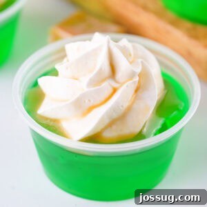 Square image of a caramel apple jello shot topped with whipped cream and caramel drizzle, perfect for social media sharing.