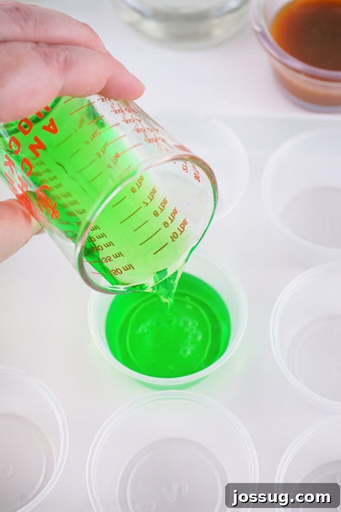 Green jello mixture being poured into small clear plastic shot cups from a measuring cup.