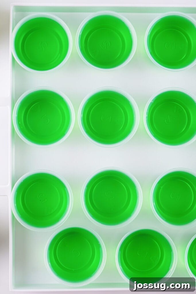 Tray of small plastic cups filled with bright green jello setting in neat rows.