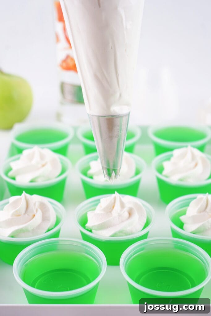 Piping bag fitted with a star tip adding whipped topping to the set green jello shots.