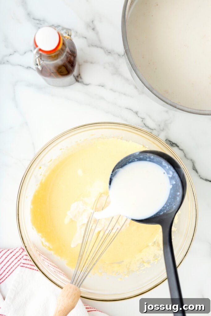 Classic Homemade Eggnog 11 Warm milk mixture being ladled into the egg yolk mixture while whisking.
