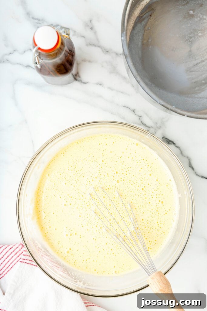 Classic Homemade Eggnog 13 Whisk resting in a bowl of tempered egg and milk mixture, smooth and frothy on top.