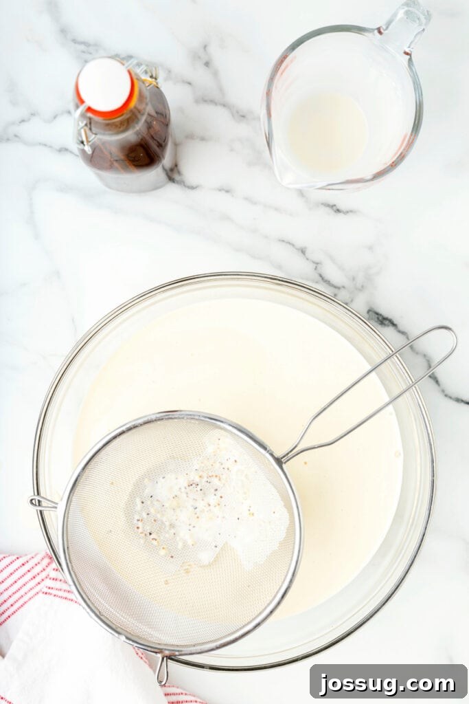 Classic Homemade Eggnog 18 Mesh strainer catching spices and solids as eggnog passes through into a glass bowl.