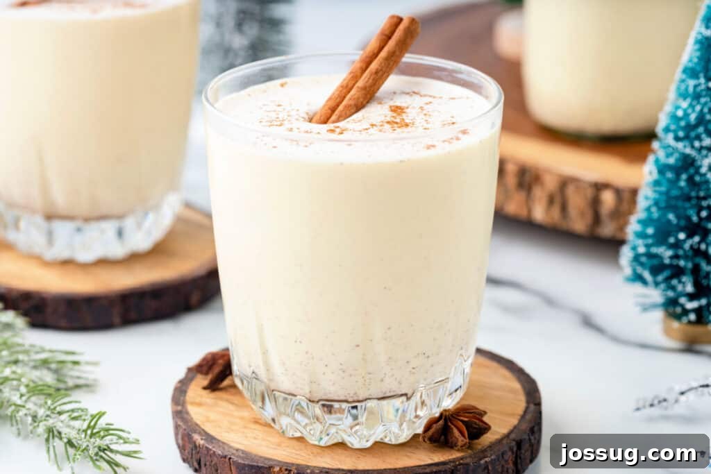 Classic Homemade Eggnog 20 Glass of homemade eggnog topped with ground nutmeg and a cinnamon stick, served on a wood coaster with festive holiday décor.