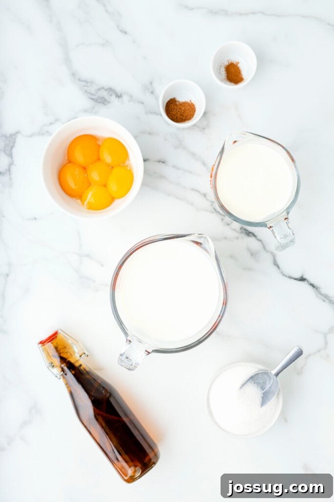 Classic Homemade Eggnog 3 Overhead view of eggnog ingredients including egg yolks in a bowl, sugar, milk, cream, spices, and vanilla on a marble counter.