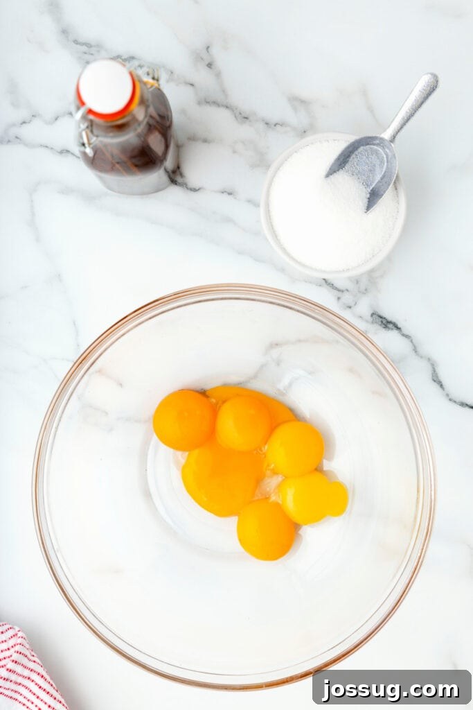 Classic Homemade Eggnog 4 Glass bowl with raw egg yolks ready to be mixed, with sugar and vanilla nearby on the counter.
