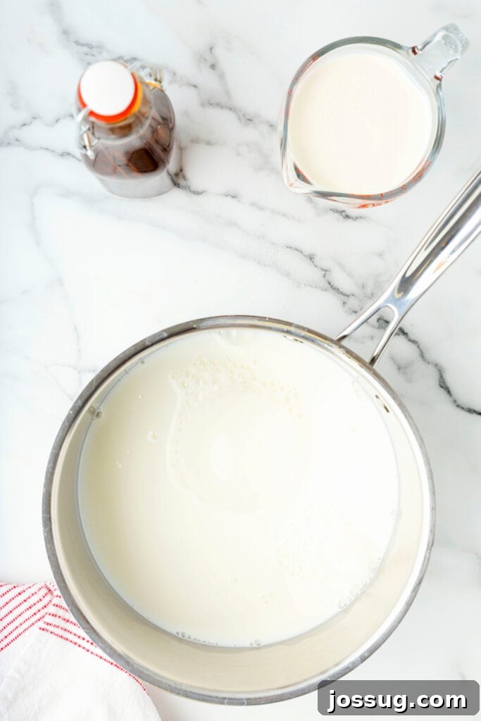 Classic Homemade Eggnog 7 Saucepan filled with milk heating on the stove, with vanilla and cream nearby.