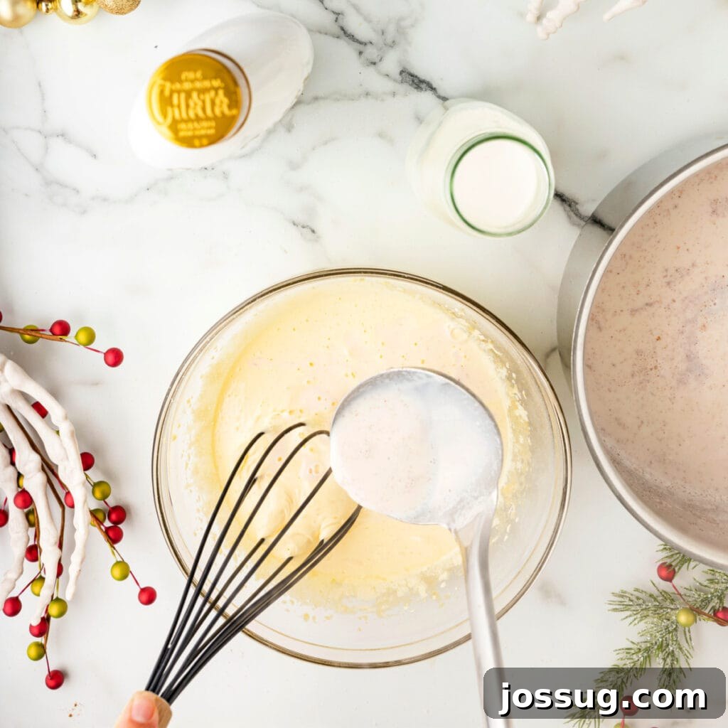 Whisk tempering egg yolks as a ladle pours warm spiced milk mixture into the bowl.