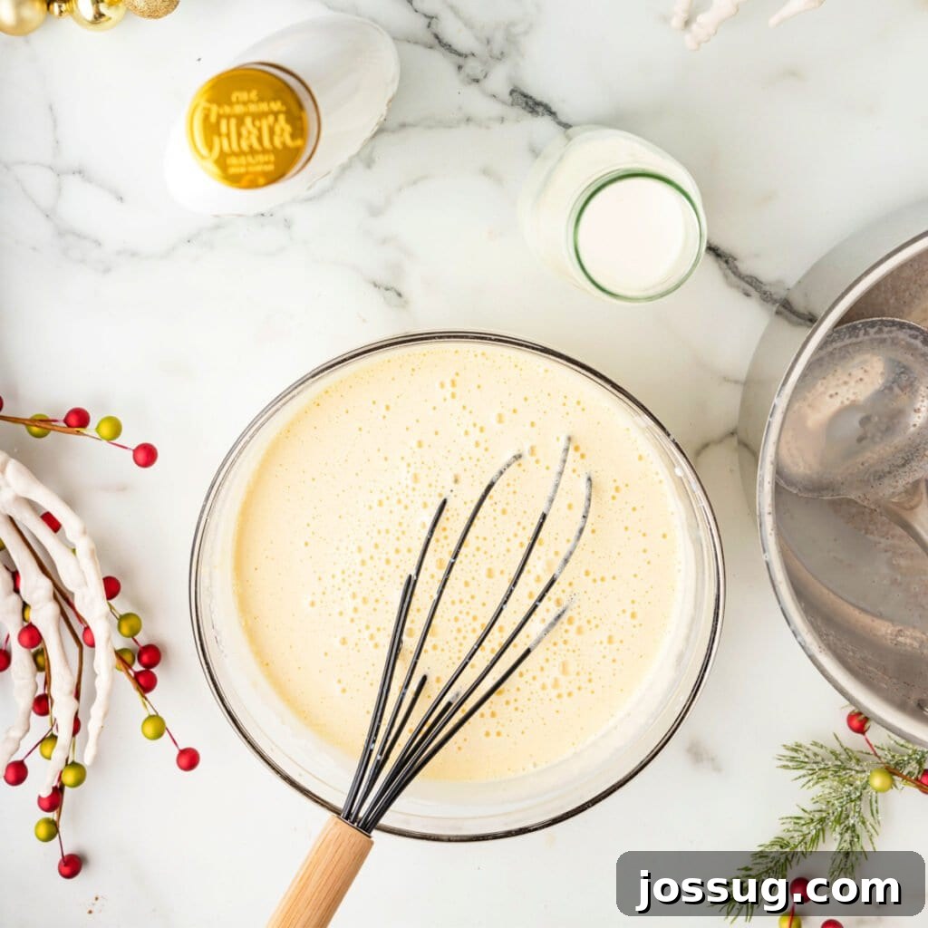 Bowl of tempered eggnog base whisked until smooth and combined, surrounded by festive greenery and holiday accents.