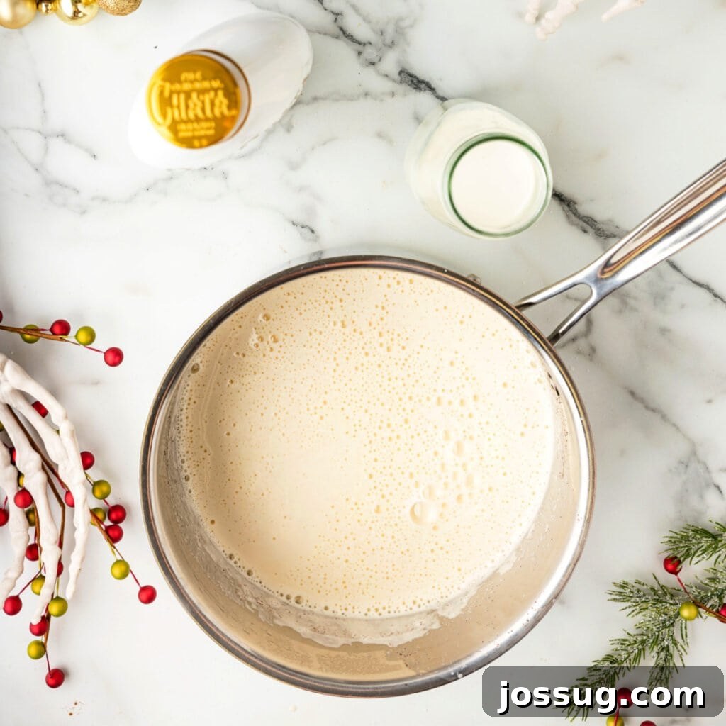 Saucepan filled with smooth, foamy eggnog base after cooking, resting on marble with festive decor nearby.