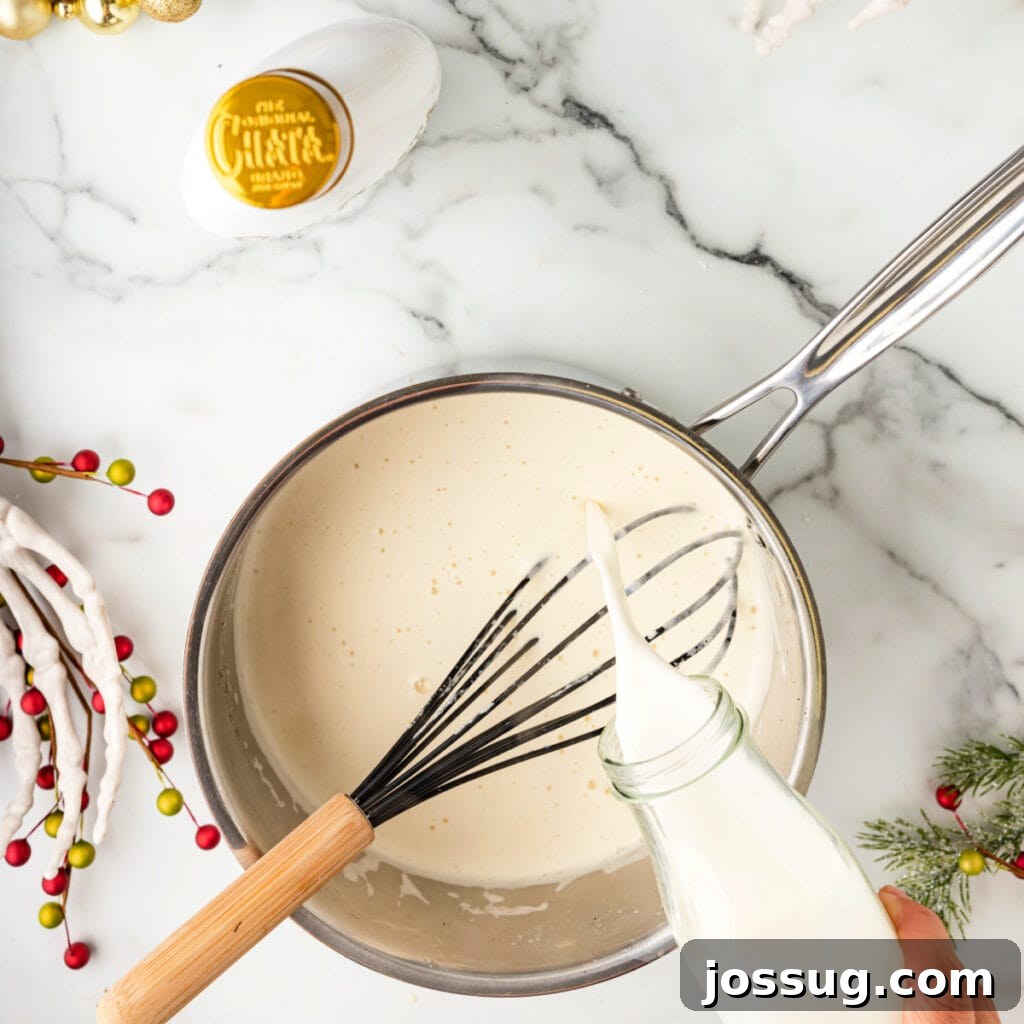 Hand pouring cream into a saucepan of warm eggnog mixture while whisking.