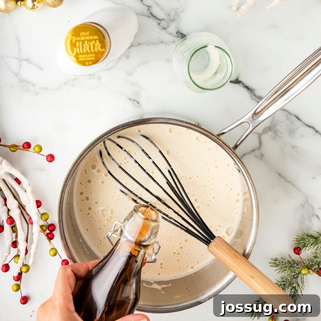 Hand pouring vanilla extract into a saucepan of cooked eggnog mixture with a whisk resting inside.