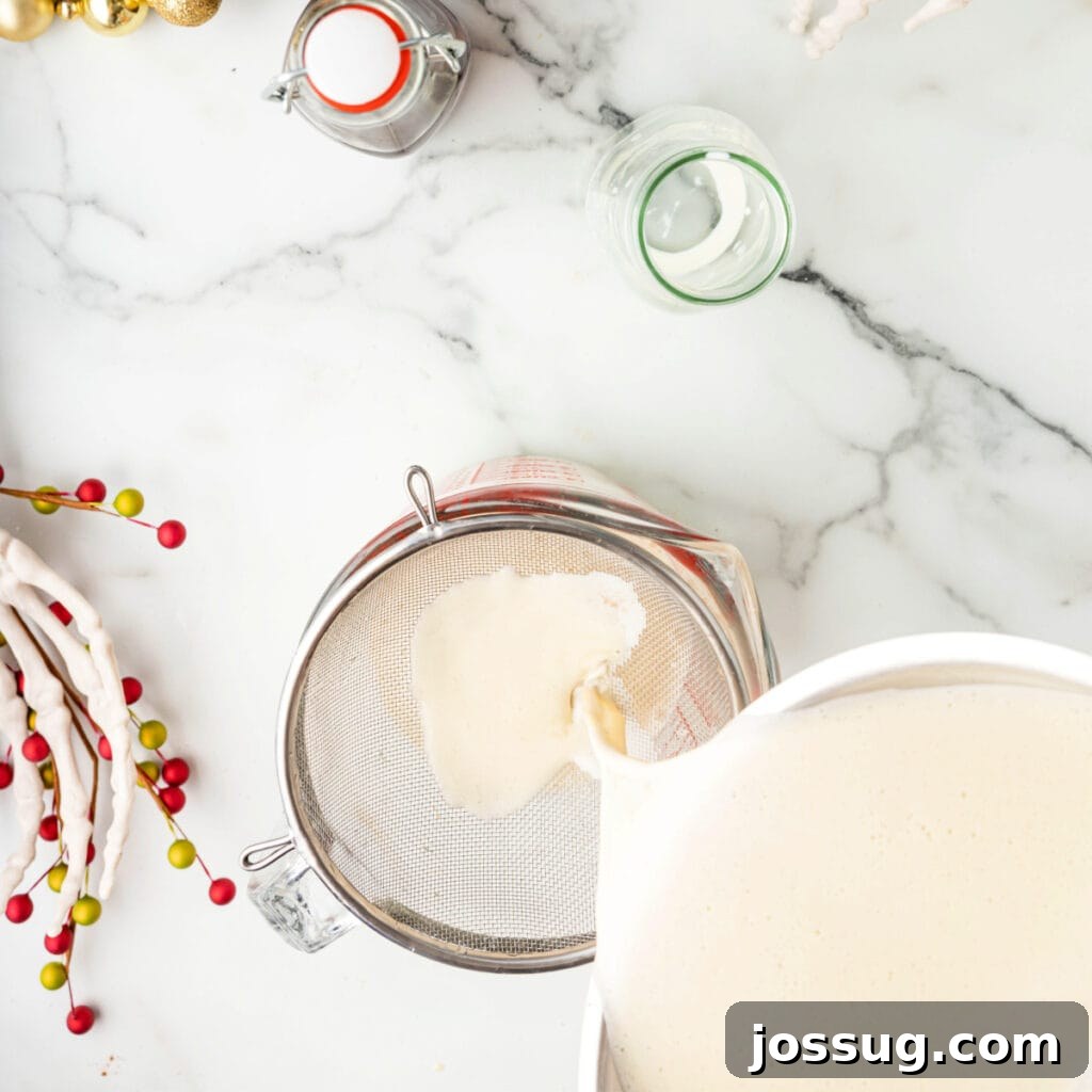 Straining eggnog base through a fine mesh strainer into a glass measuring cup.