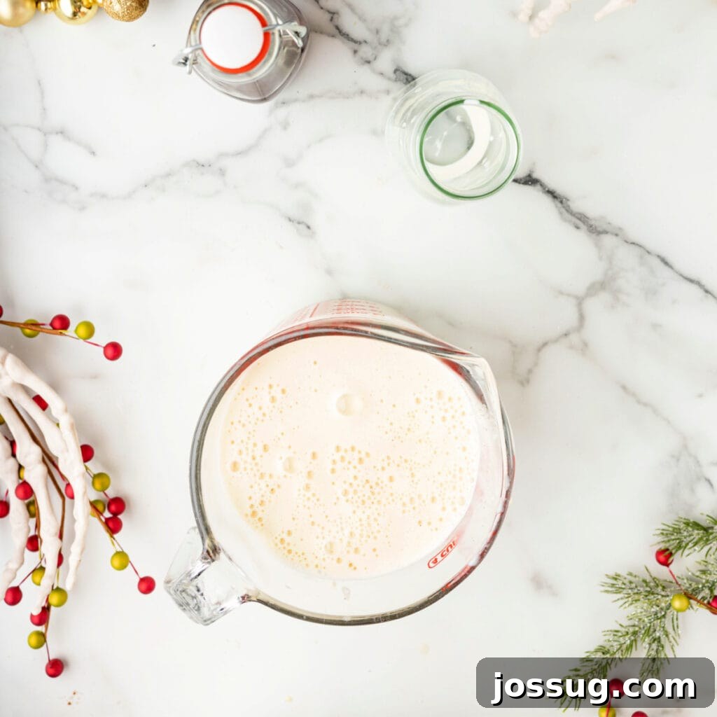 Freshly strained eggnog base in a glass measuring cup with bubbles on the surface.