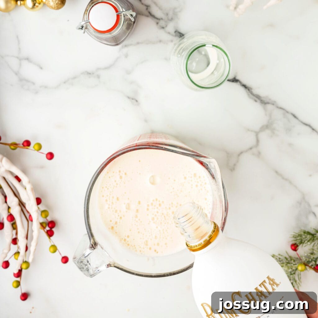 Hand pouring RumChata into a glass measuring cup filled with cooled eggnog base.