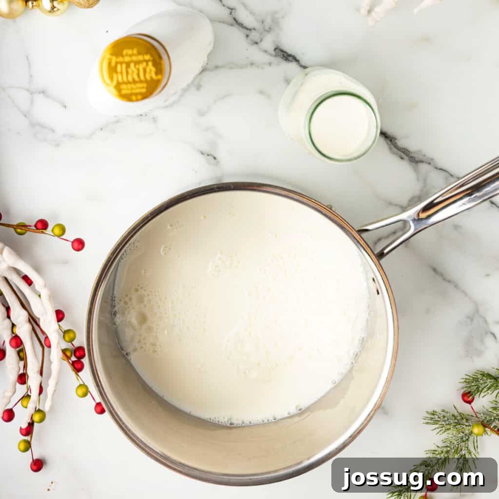 Saucepan filled with milk heating on the stove, RumChata and cream jar nearby on a marble surface with holiday decor.