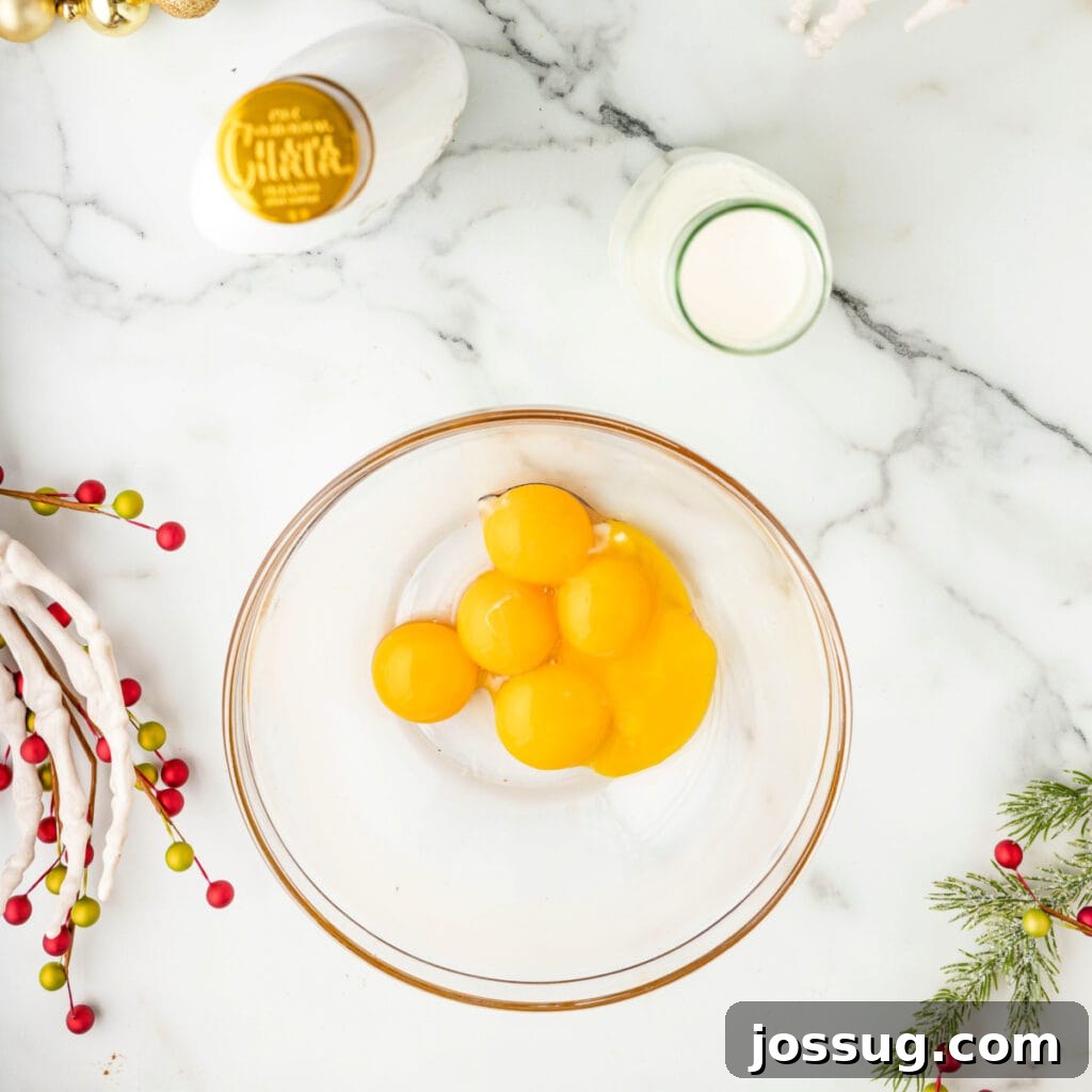 Bowl with raw egg yolks set on a marble counter next to cream and RumChata.