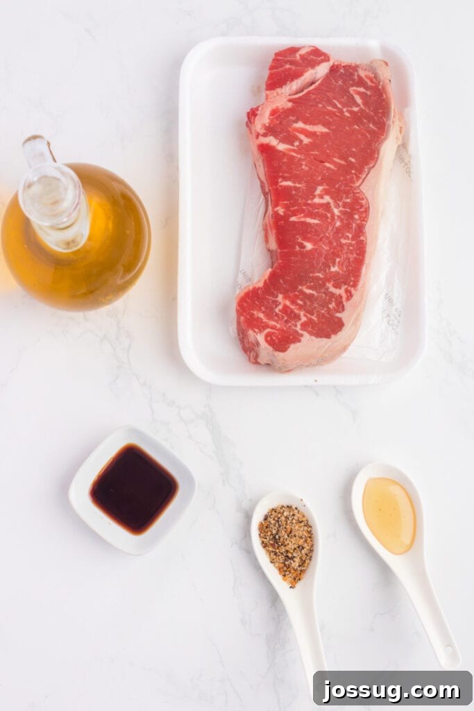 Crispy Air Fryer Steak Bites 3 Raw strip steak with olive oil, soy sauce, honey, and Montreal steak seasoning displayed on a white surface, showcasing the fresh ingredients.