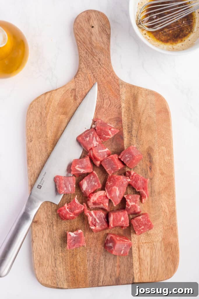 Crispy Air Fryer Steak Bites 5 Sirloin steak cut into uniform cubes on a wooden cutting board with a knife and marinade bowl nearby, demonstrating proper preparation.