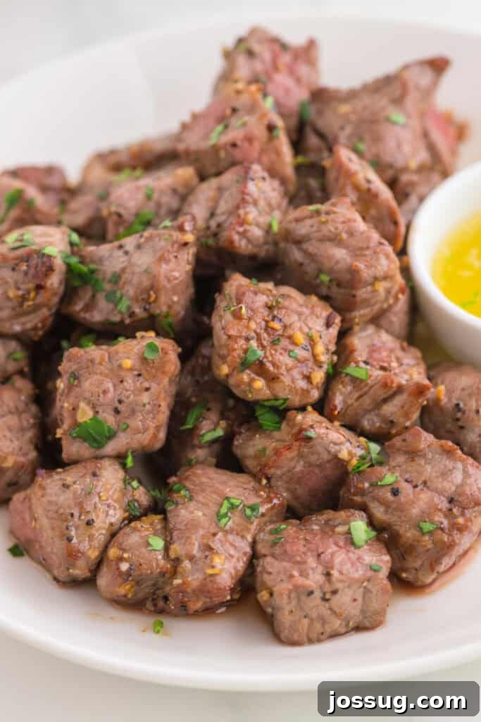 Crispy Air Fryer Steak Bites 9 A plate of perfectly cooked steak bites garnished with fresh parsley and served with a side of rich garlic butter dipping sauce, presenting a complete meal.