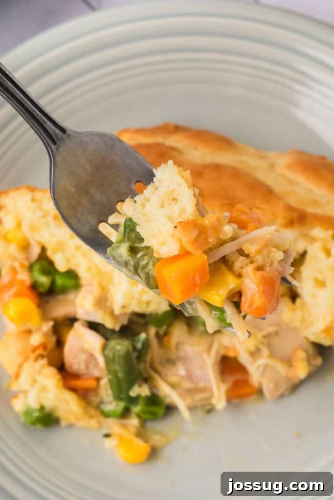 Fork lifting a bite of Chicken Biscuit Pot Pie with biscuit topping, chicken, carrots, peas, and corn in a creamy sauce.