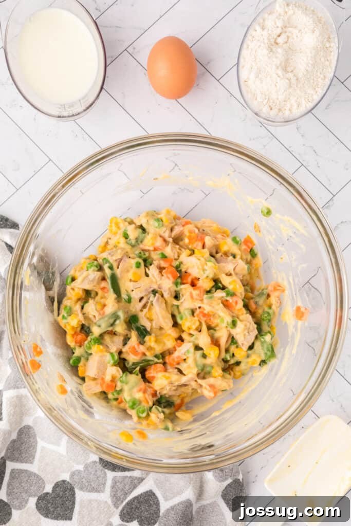 Mixed chicken, vegetables, and soup creating a creamy Chicken Biscuit Pot Pie filling in a glass bowl.