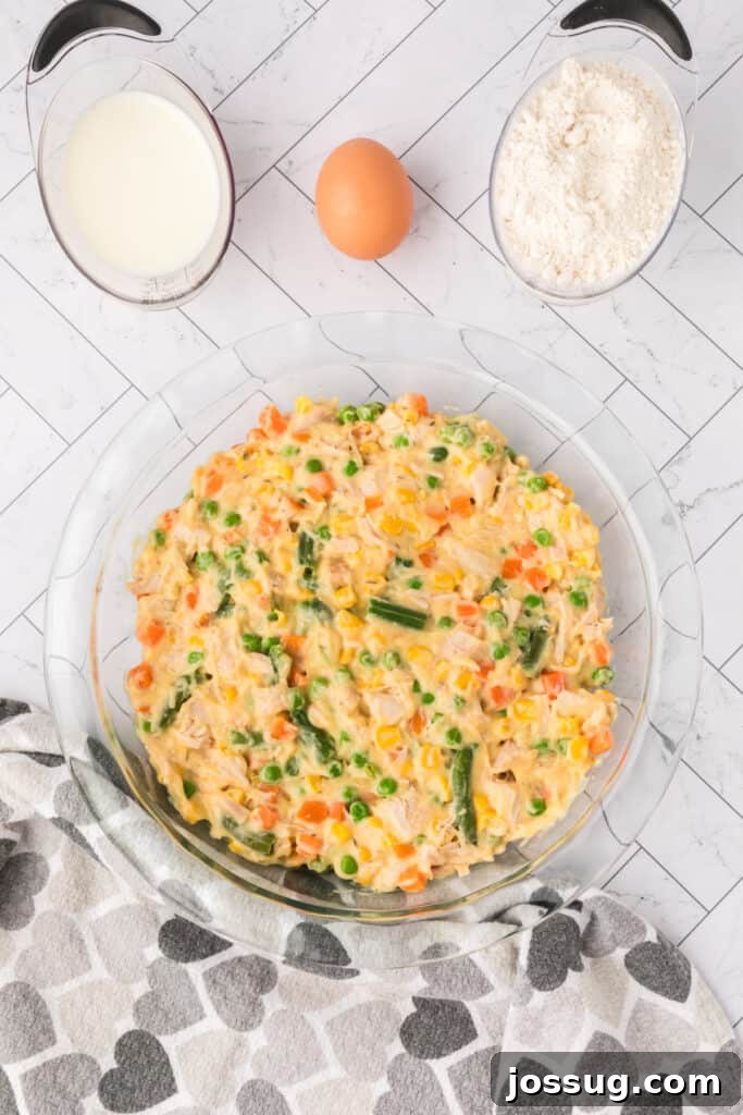Chicken pot pie filling spread evenly in a clear pie dish before adding biscuit topping.