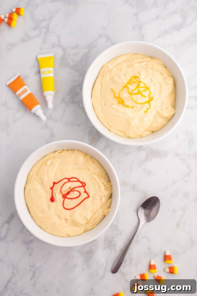 Two bowls of cupcake batter with yellow and orange gel food coloring drizzled on top before stirring.