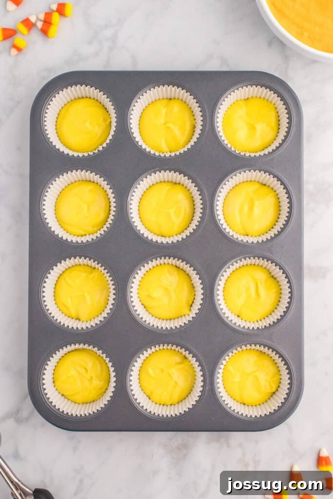 Cupcake liners partially filled with yellow batter as the first layer for Candy Corn Cupcakes.