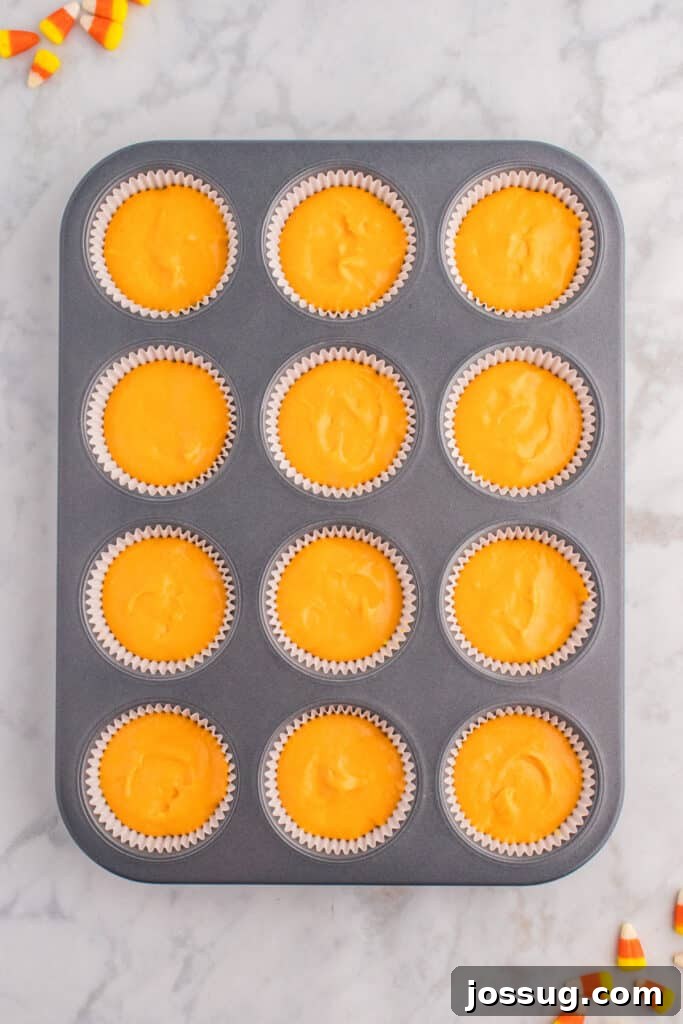 Cupcake liners now filled with orange batter on top of yellow layer before baking.